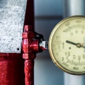 Detailed view of a pressure gauge attached to a red industrial pipe, measuring PSI and kPa.